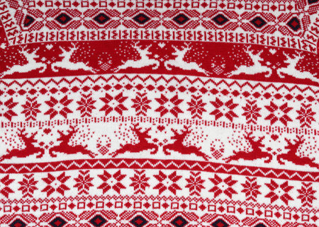 close-up of a scandinavian knitted fabric with a traditional Christmas ornament: red reindeer and...