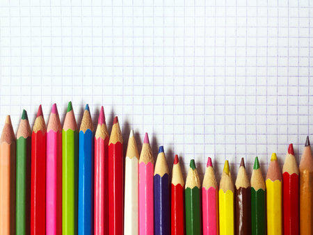Many colored pencils on a white notebook sheet in a cage, arranged as a wave. There is a place for...