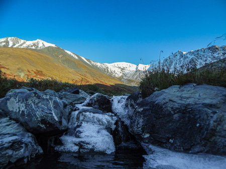 Stream with stones covered with ice on the background of snow mountains