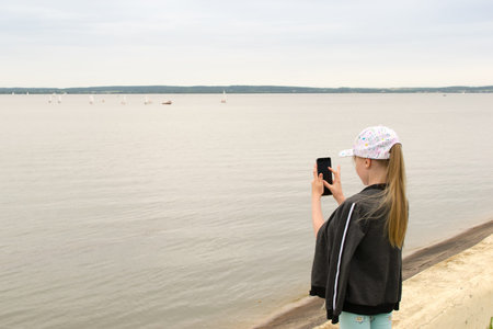 girl takes pictures of sailboats at sea on her phone