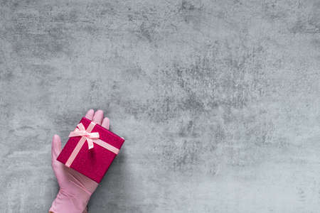 Love gift. Valentine day greeting. protection. Hand in medicine glove holding red present box on gray copy space. Advertising background.の写真素材