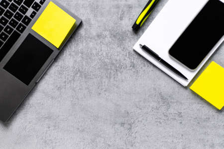 Laptop, phone, and office supplies on a gray concrete table. Workplace. A study table. Remote work. Distance learning. uminous yellow and extremely gray. The color of 2021. Copy spaceの写真素材
