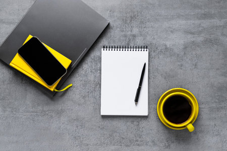 Laptop, phone, and office supplies on a gray concrete table. Coffee in a yellow cup. Workplace. A...