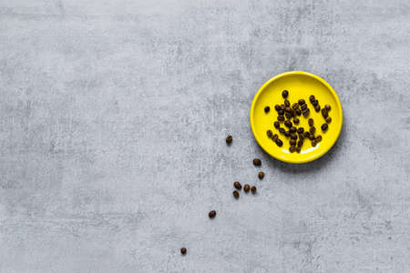 Coffee beans on a yellow plate, scattered grains on a gray concrete tableの写真素材