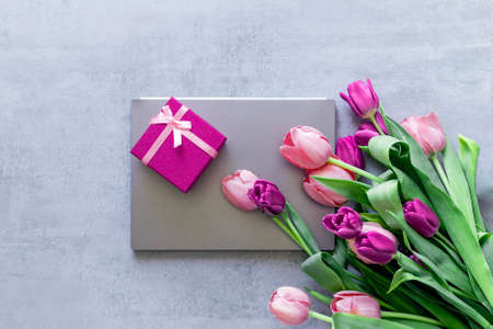 A gray laptop, a pink gift box, and a bouquet of tulips on a gray concrete background. Giftの写真素材