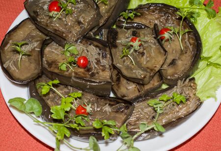 Fried eggplant slices with garlic and cherry tomatoes on a plateの写真素材