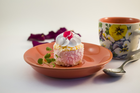 Small cake with cream, cherries and coconut topping on a ceramic plateの写真素材