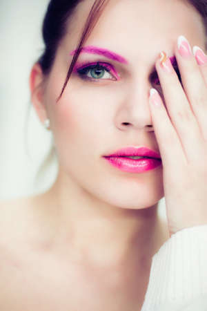 The woman with a bright pink make-up closes one eye a hand. Studio portrait.の写真素材