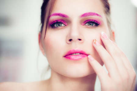 The woman with a bright pink make-up touches with a hand a cheek. Studio portrait.の写真素材