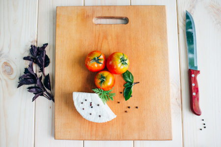 tomatoes, knife, pepper,basil and homemade cheese on light rustic wooden board, top view. Culinary backgroundの写真素材