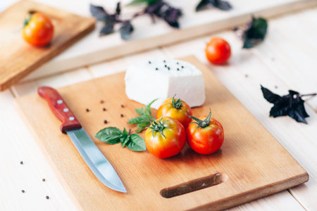 mediterranean cuisine: tomatoes, knife, pepper,basil and homemade cheese on light rustic wooden board, top view. Culinary italian backgroundの写真素材