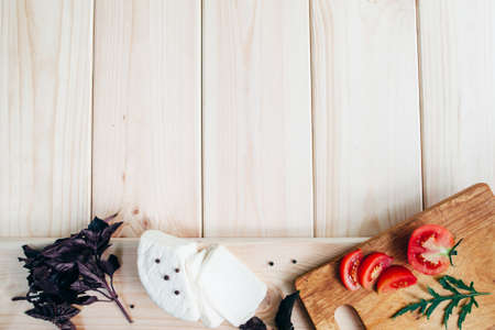tomatoes, knife, pepper,basil and homemade cheese on light rustic wooden board, top view. Culinary italian backgroundの写真素材