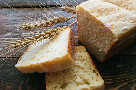 Slices of white loaf and cones of wheat on a dark wooden background