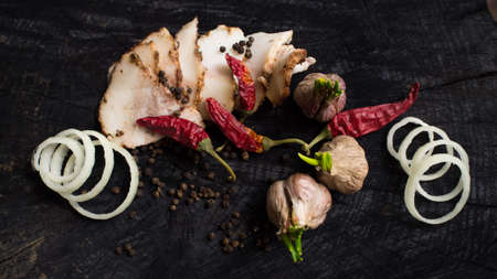Bacon, garlic, onions and pepper on a dark wooden tableの写真素材
