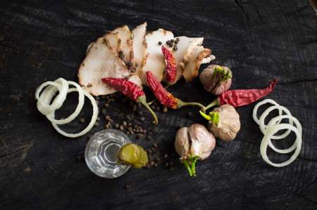 Bacon, garlic, onions, pepper and vodka on a dark wooden tableの写真素材
