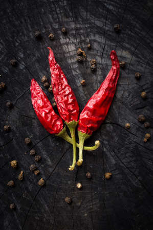 Some hot red peppers and black pepper lie on a dark boardの写真素材