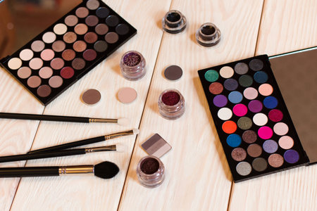 collection of cosmetics for make-up artist. Bright and neutral eye shadows, pigments, glitter and eyeliner. studio photo on a wooden background. top view.