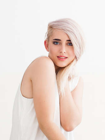 confident blonde with big blue eyes, bright eyebrows. She's flirting, smiling, fooling around with her hair and looking at the camera. studio photo on white background.の写真素材