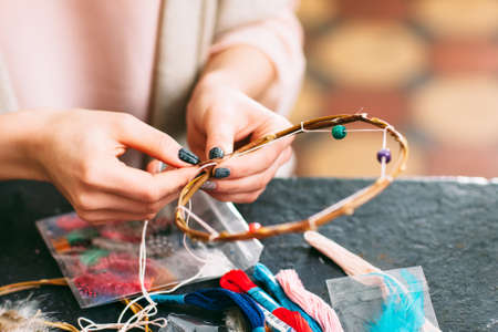 craftswoman makes Dreamcatcher of sewing accessories  in art studio. Side view on workshop table and hands.の写真素材