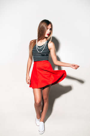 Stylish hipster girl in new  bright red skirt posing on white background. She walk and her skirt flying.の写真素材
