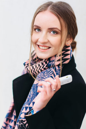 The potrait of a pretty smiling girl in a black coat with a white mobile phone