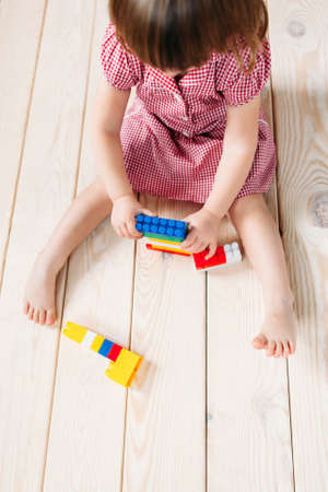 little girl in red dress sitting on the wooden floor and playing Lego. Top viewの写真素材