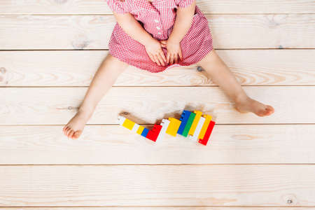 little girl in red dress sitting on the wooden floor and playing Lego. Top viewの写真素材