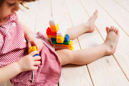 little girl in red dress sitting on the wooden floor and playing Lego. Top viewの写真素材