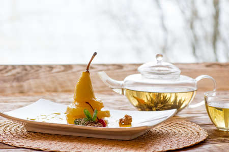 Pear in an orange juice on a whire square plate with a herbal tea. Vegetarian's dessert.の写真素材