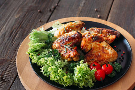 Grilled chicken wings with fresh vegetables. Baked chicken meat with lettuce and tomatoes cherry. Homemade meat on wooden table.の写真素材