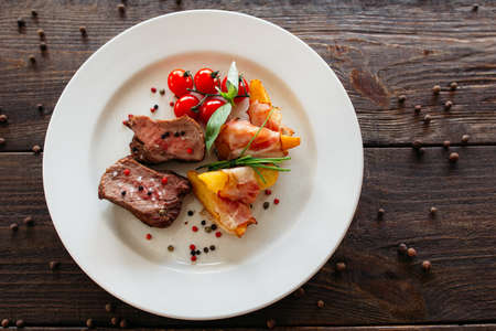 Medium rare pork steak with fresh vegetables. Food photography of pork steak with potatoes and tomatoes cherry. Tasty cook meat with vegetables on dark wooden background.の写真素材