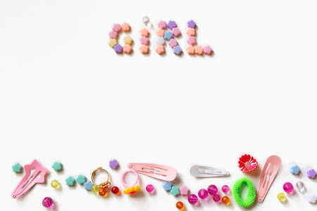 Little girl accessories lifestyle set on  white background.  Many little girl accessories scattered on blank white paper - beads, hair clips, rings. There are the inscription Girl on the top of imageの写真素材