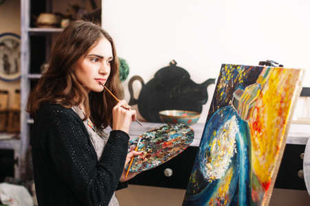 Creative pensive  painter paints a colorful picture. Closeup of painting process in art workshop Creative positive woman painter paints in her studio abstract picture.の写真素材