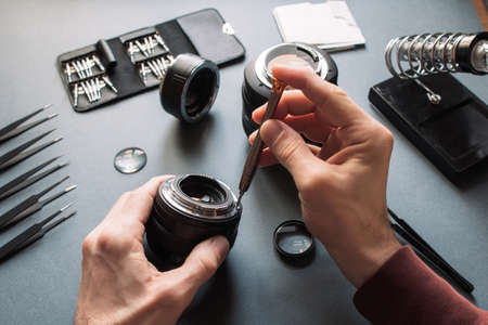 Photo camera lens repair set. Technician engineer check optics alignment and maintenance support of broken photographic 50 1.4 photo camera lens part. Pov to workplace and engineer's hands.の写真素材