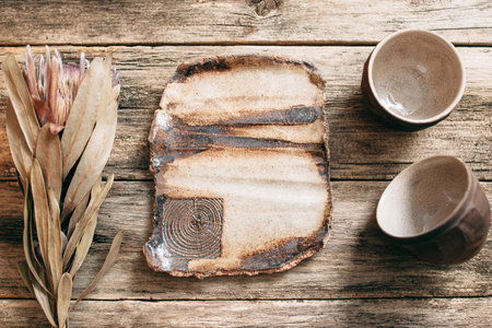 Rustic creative brown pottery empty big dish on wooden table. Handmade beige ceramics with nature pattern. Empty clay plate and bowl on old wooden background with freee space on plateの写真素材