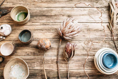 Flat lay set of handmade modern ceramic crockery. Top view of unusual creative bowls with rare dry flowers on  old wooden background. Beige and blue empty ceramics over wooden table with free spaceの写真素材