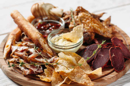 Beer snacks plate, red and yellow sauces on wooden board. Meat, cheese and chips on white background. Closeup of beer snacks setの写真素材