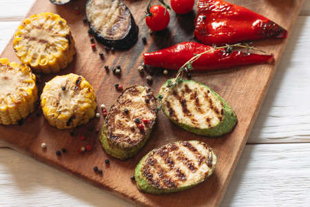 Delicious grilled vegetables on cutting board. Flat lay of close-up corn, pepper, vegetable marrow, eggplant on wooden background.の写真素材