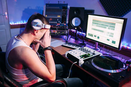 Tired DJ after hard work in sound recording studio. Exhausted DJ after overtime, he has problems and headache. Tired sound producer hiding his eyes.の写真素材