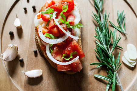 Tomato with onion sandwich flat lay. Vegetable sandwich with tomato and onion. Close-up of vegetarian sandwich on wooden catering plate decorated with garlic and rosemaryの写真素材
