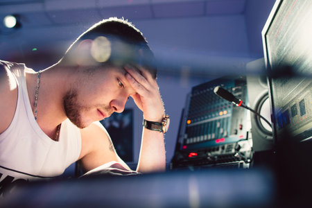 Tired dj sitting at studio near his sound equipment close-up. View on head and shoulders of young...