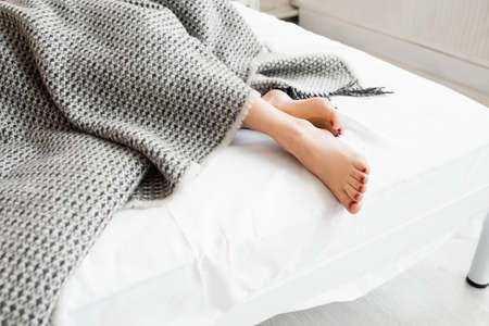 Woman feet under gray blanket sideview. Beautiful young woman feet with red pedicure on the bed. Sleeping woman legs under the gray blanketの写真素材