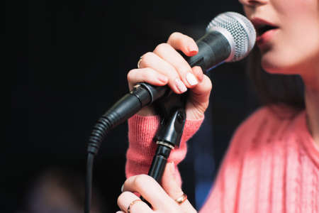 Microphone and unrecognizable female singer close up. Cropped image of female singer in pink dress , singing into a microphone, holding mic with two hands. Copyspaceの写真素材