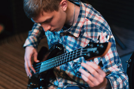 Musician tuning strings on his bass-guitar. Front view on bass player spinning guitar tuners....