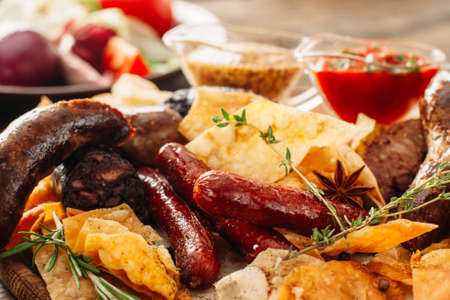 Closeup of beer snacks set. Assorted chips and sausages with red and yellow sauces. Colorful tasty beer snacks setの写真素材