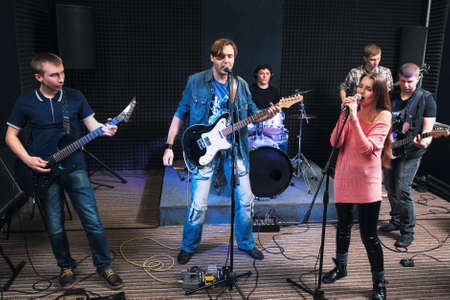 Music band alive performance on stage. Two vocalists sing, other member play on their musical instruments. Music group play their song.の写真素材