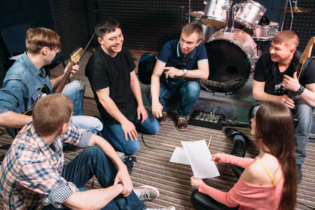 Musicians learning new song on the floor. Top view on music band members sitting on the floor with song text. Vocalist smiling at woman. Lifestile of young people group. Teamwork.の写真素材