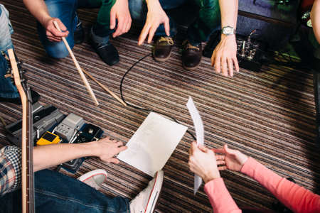 Musical discussion spot . Top view on musicians leg, sitting in circle, around the sheet of paper with song text.の写真素材