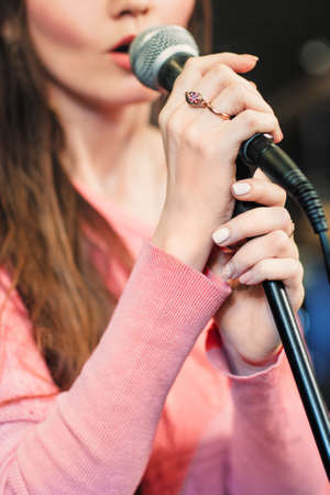 Closeup of singing caucasian woman. Young unrecognizable woman emotionally sings into the microphone, holding it with two hands.の写真素材