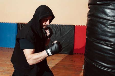 Man training with punching bag at gym. Profile of boxer workout with punching bag. Moment before kicking punching bag by sportsman in black sportsuitの写真素材